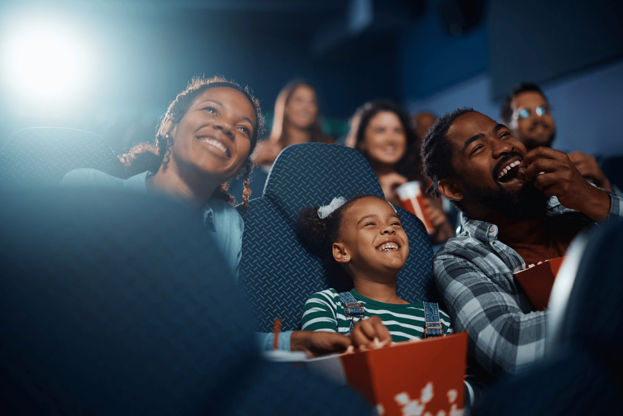 Vue International + Pearl-Plaza: image of a family consisting of a mother, child and father smiling while watching a moving in a movie theater and eating popcorn